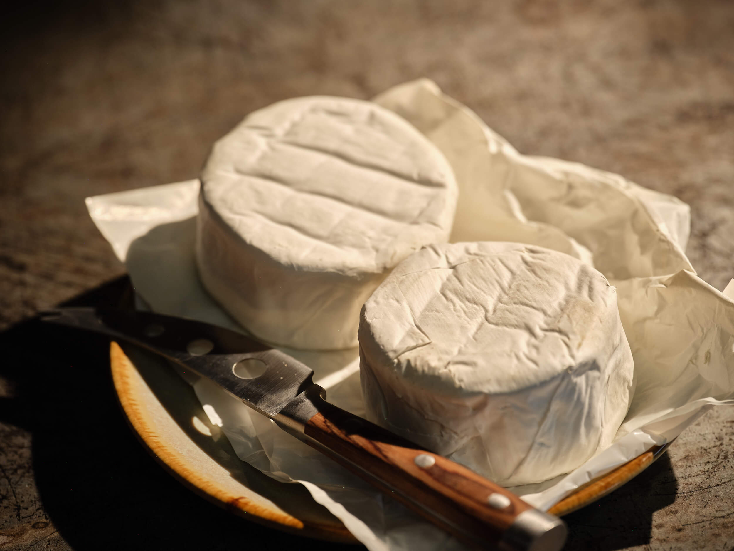 Two sets of Bruton Brie Cheese presented on a rustic dish with a cheese knife.