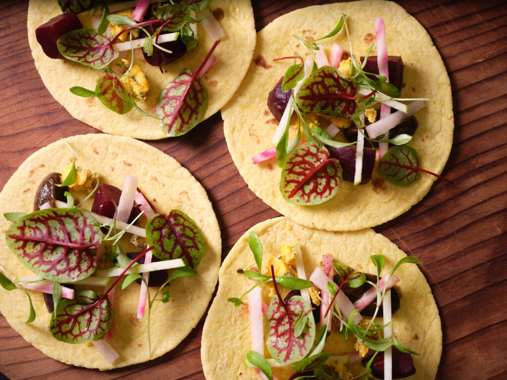 Four Yarlington Blue Tacos on a wooden board with fresh salad leaves.