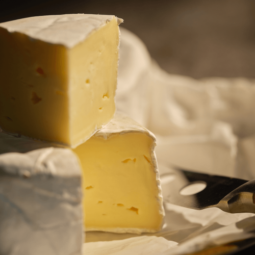 Circular Bruton Brie presented on a wooden board, with one piece sliced.