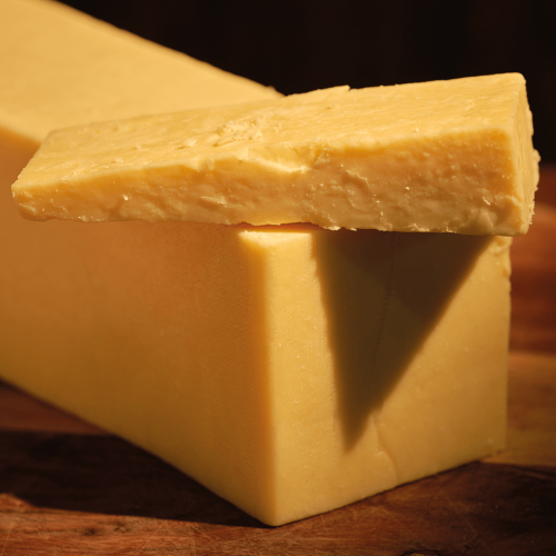 Greens of Glastonbury Twanger Cheese with a thin triangle placed on a large block.