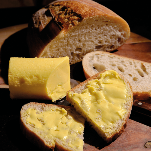 Longmans salted butter next to crusty bread, with two pieces buttered.