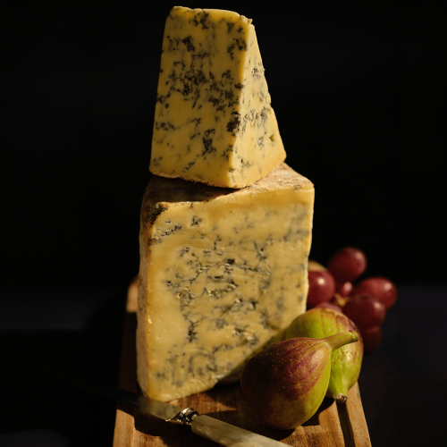 Yarlington Blue Cheese stacked up with fruit, with a black background.
